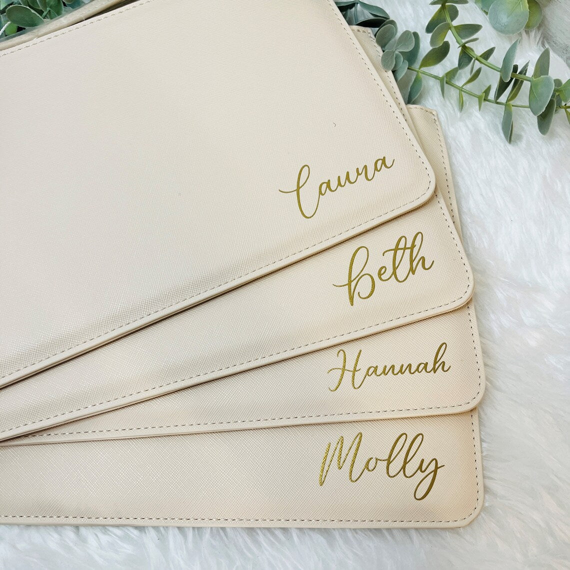 A stack of beige clutch bags with gold text personalisation for bridesmaids