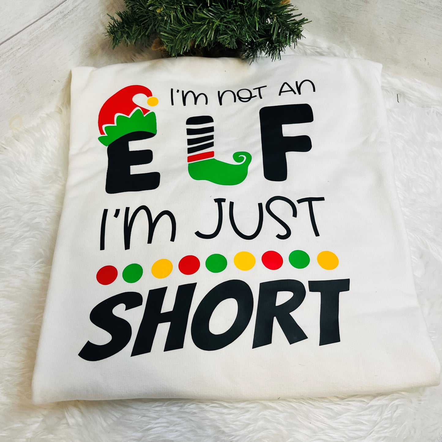 Folded Sweatshirt with 'I'm not an elf I'm just short' under a christmas tree