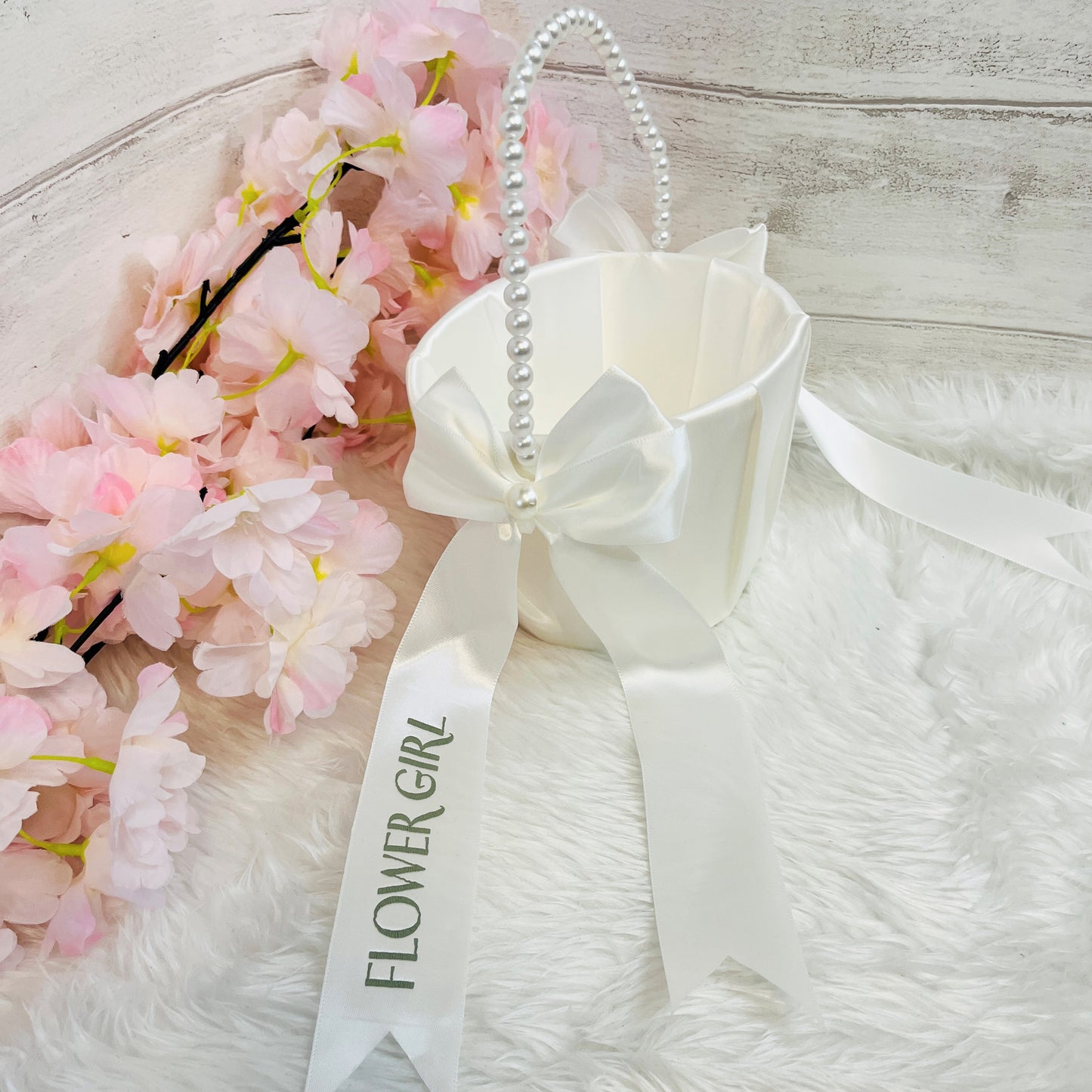 White flower girl basket with pink flowers on a white fur surface