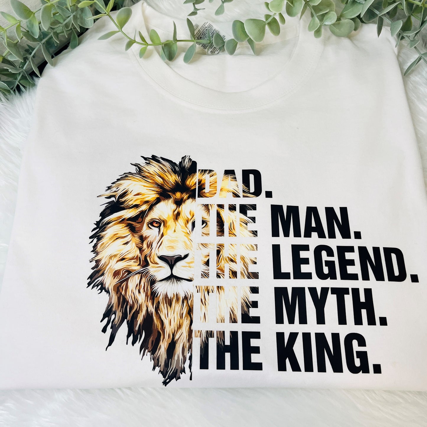 White t-shirt with a graphic print of a lion's face in two different shades, with the text 'DAD, THE MAN, THE LEGEND, THE MYTH, THE KING.'.