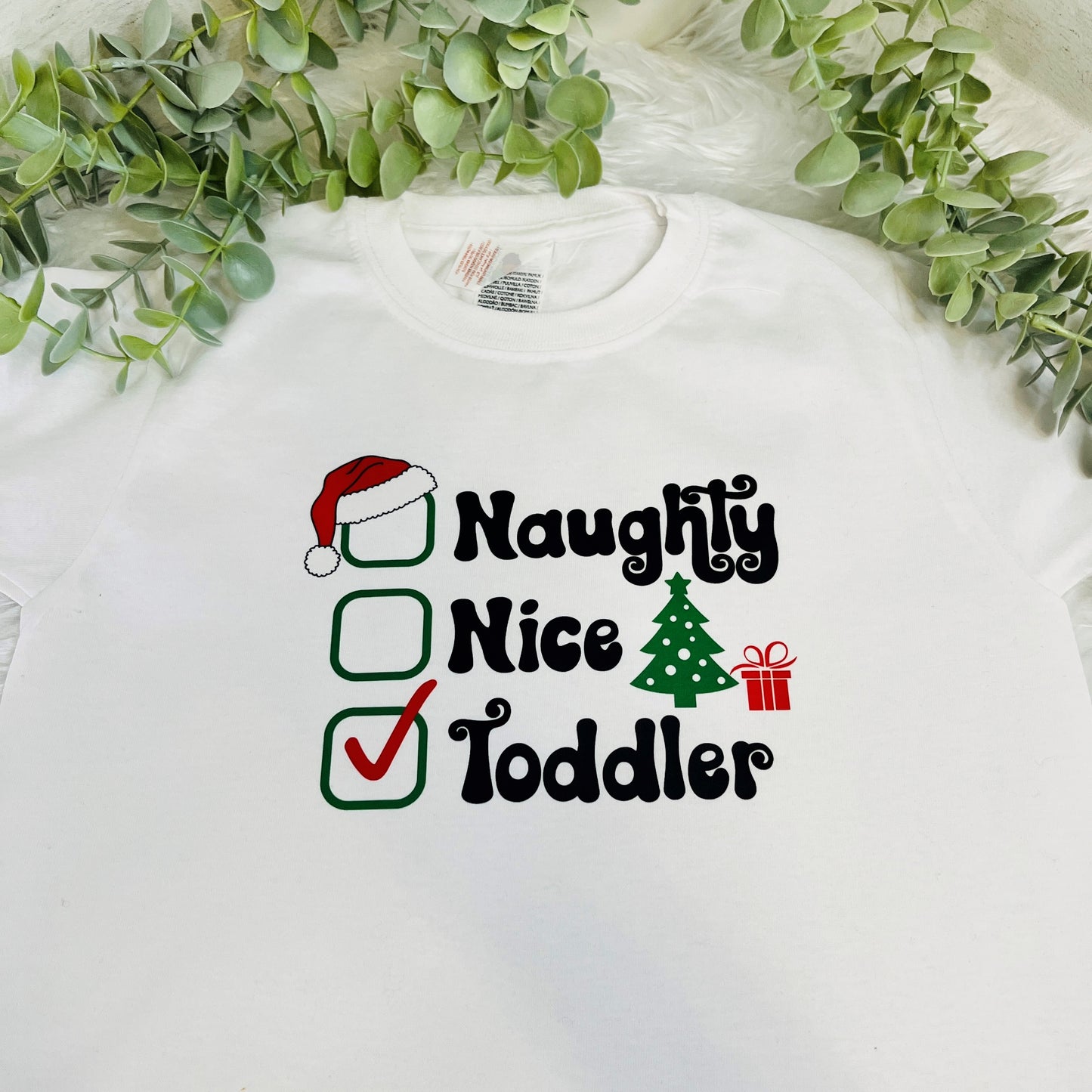 A white kids t-shirt showing the text 'naughty, nice, toddler' with a tick in the toddler box