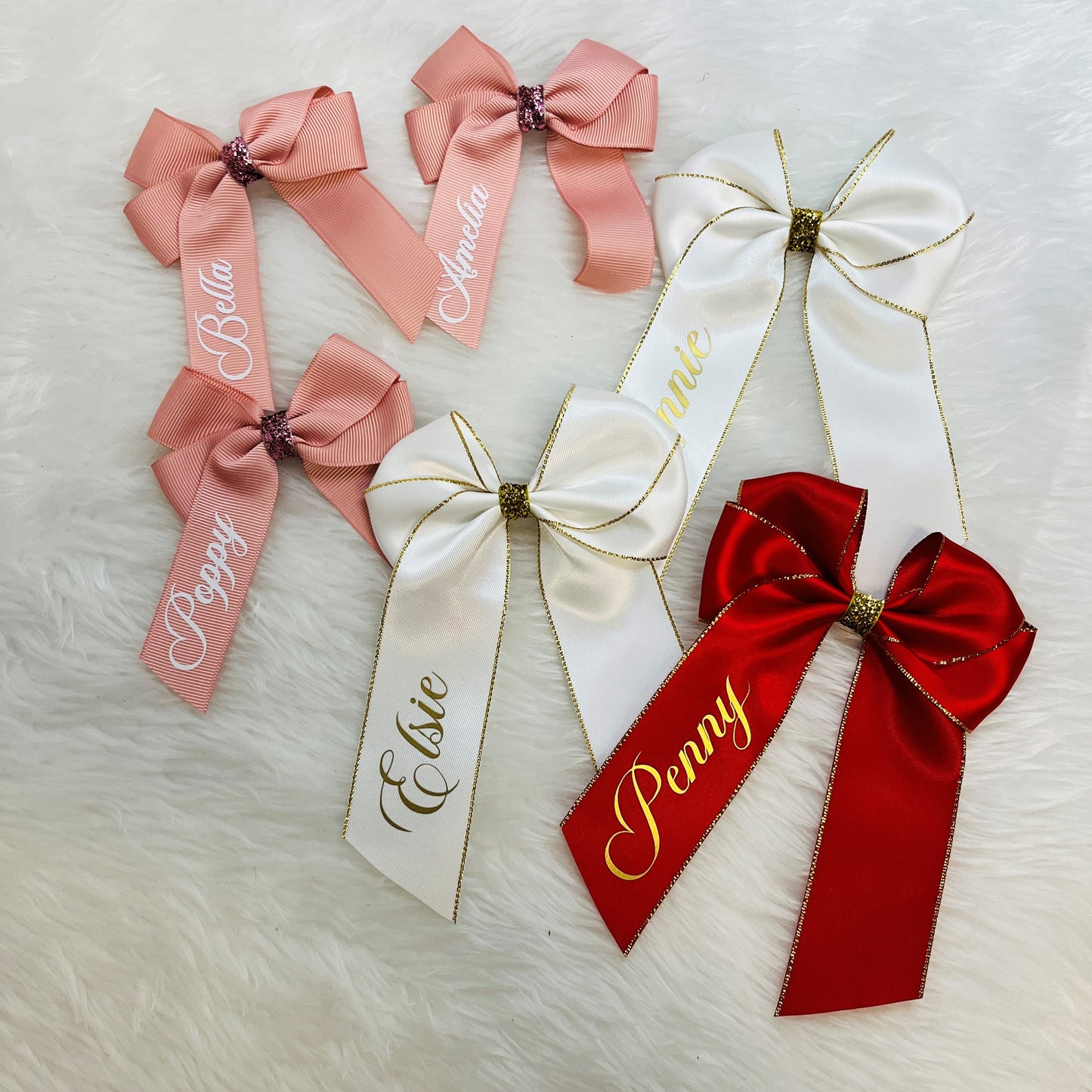 selection of satin personalised hair bows in pink, ivory and red against a white background