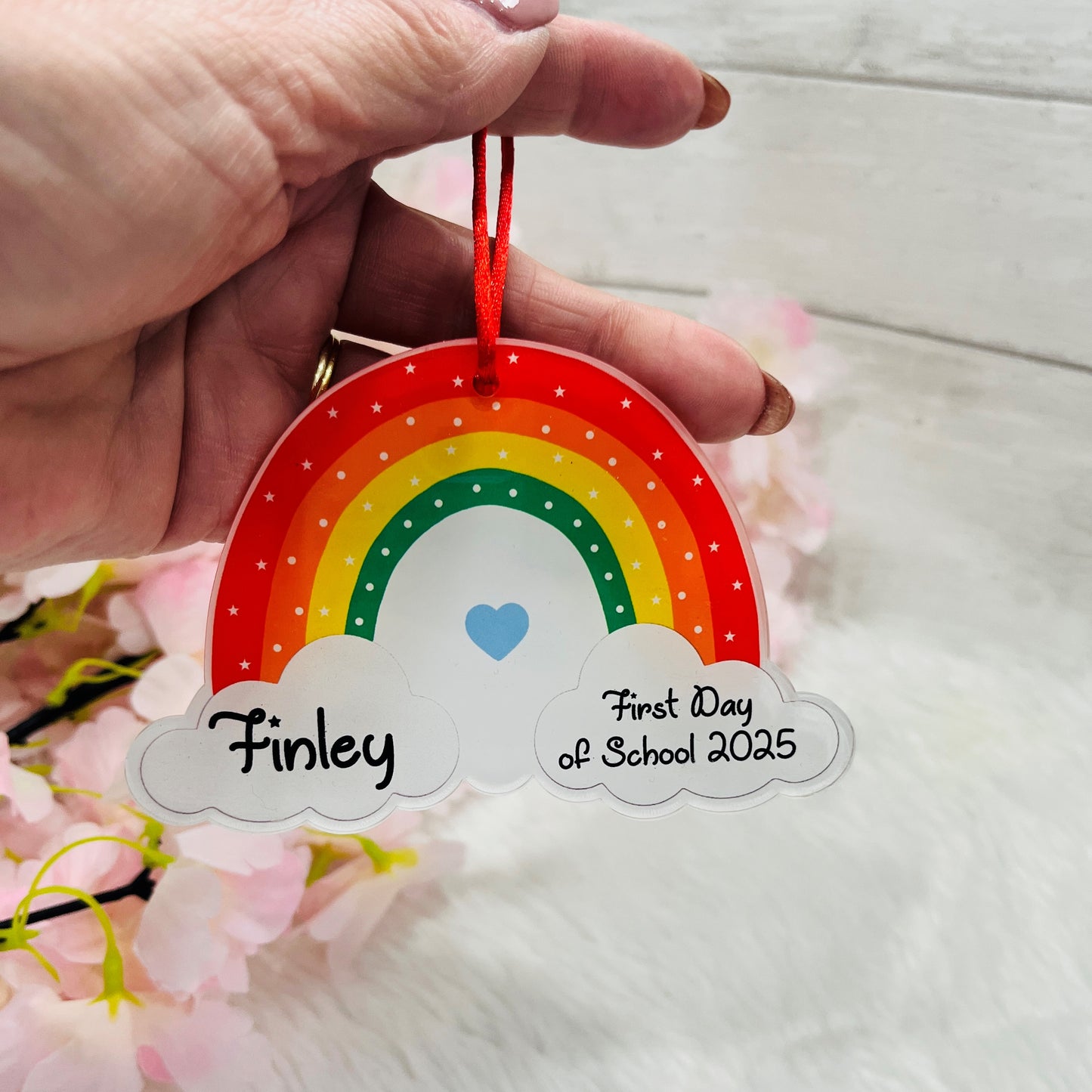 Colorful rainbow-shaped tag with 'Finley' and 'First Day of School 2025' text, held by a hand.