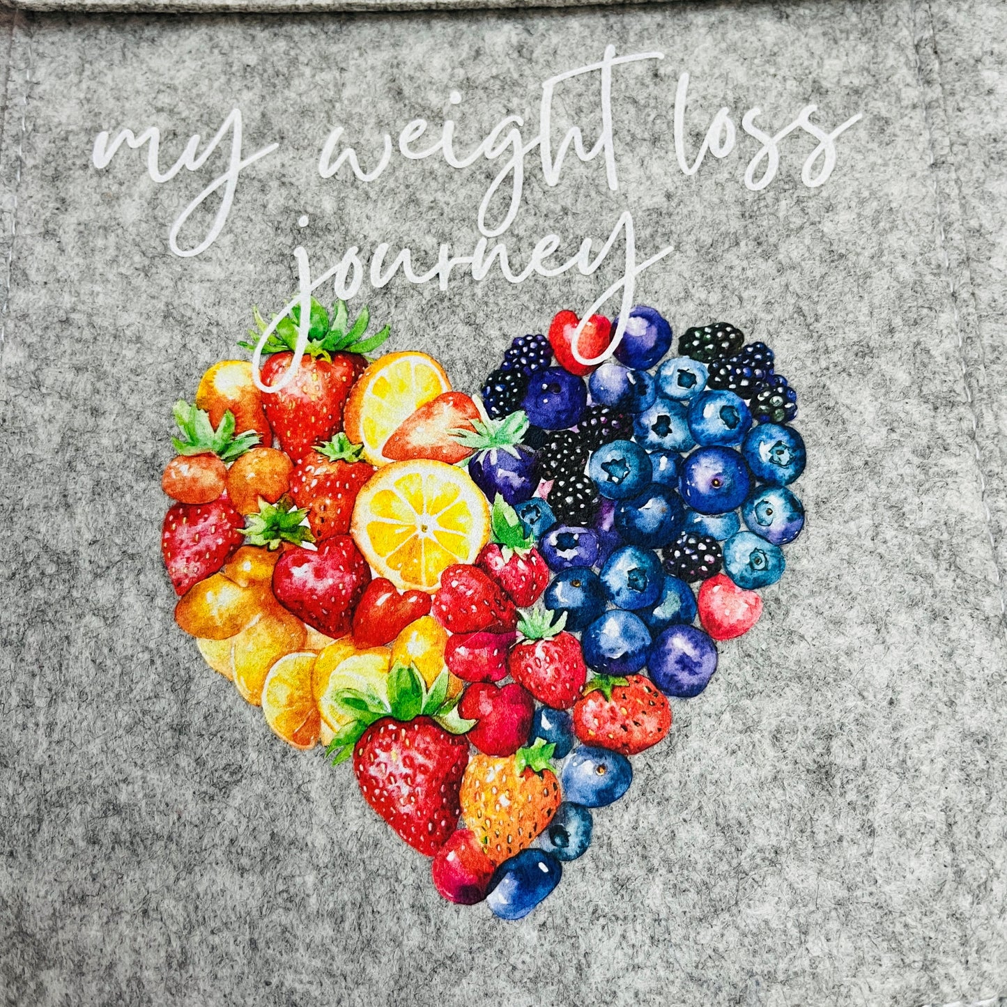 Heart-shaped arrangement of fruits on a grey background with 'my weight loss journey' text.