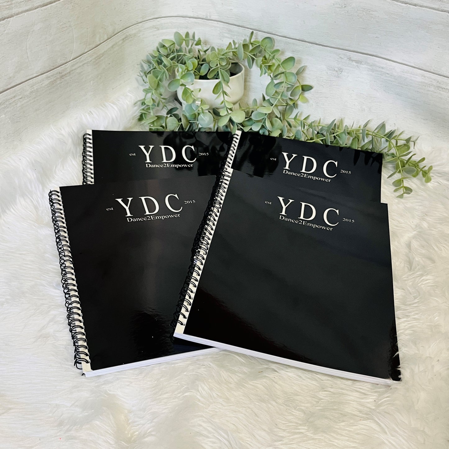 Three black notebooks with 'YDC Dance Empower' branding on a white surface with greenery.