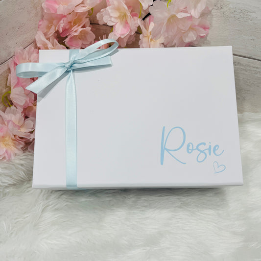 White gift box with a light blue ribbon and 'Rosie' written on it, surrounded by pink flowers.