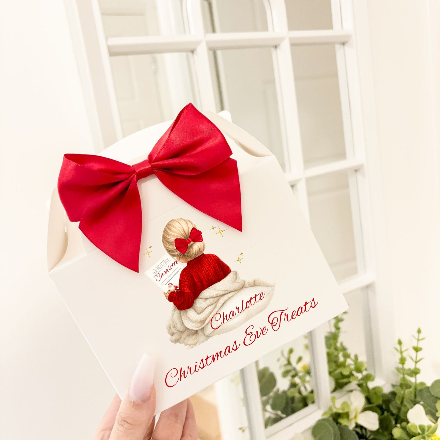 Christmas-themed treat bag with a red bow held by a hand, with a girl child design against a white lattice background.
