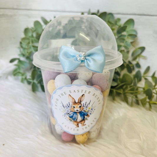 An Easter Dome Snack Pot featuring a plastic cup with a blue bunny wreath design and a blue bow on the lid, filled with various small snacks.