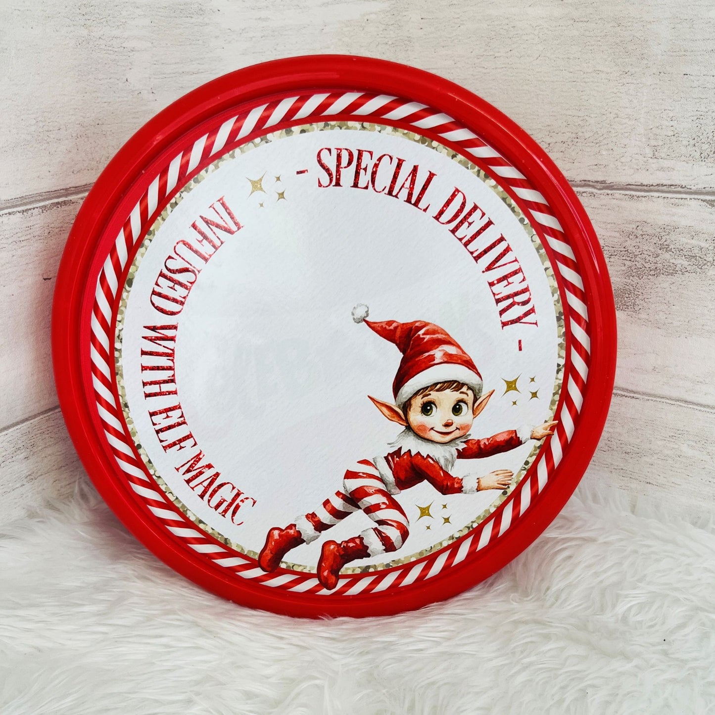 A tub of chocolates with a personalised elf design topper with the text 'special delivery - infused with elf magic' on the front and an elf illustration on a faux fur background
