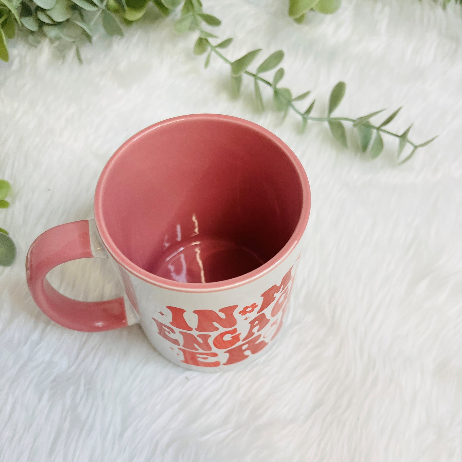 Pink mug with text on a white surface with green leaves