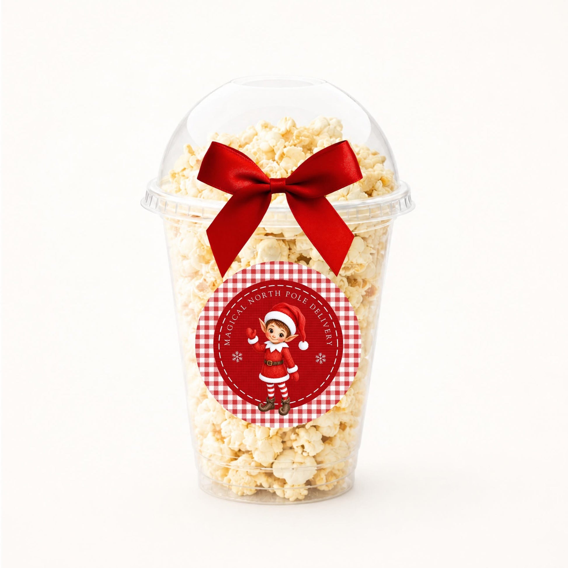 A clear plastic popcorn cup filled with popcorn and topped with a large red ribbon bow, featuring a round red-and-white christmas elf sticker on the front.