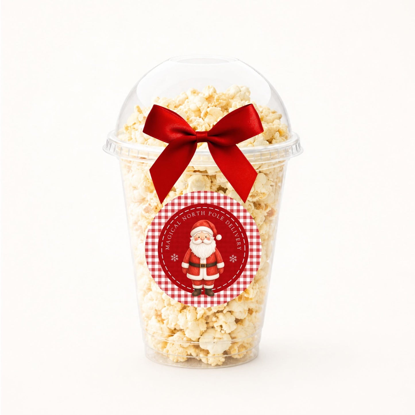 A clear plastic popcorn cup filled with popcorn and topped with a red ribbon bow, featuring a round gingham Santa-themed sticker on the front.