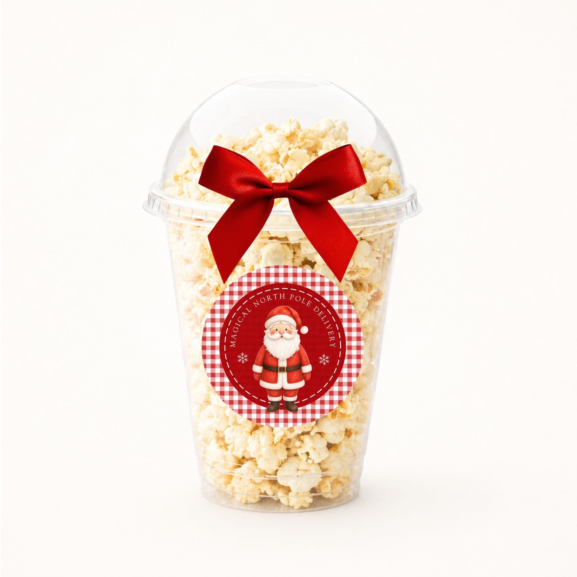 A clear plastic popcorn cup filled with popcorn and topped with a red ribbon bow, featuring a round gingham Santa-themed sticker on the front.