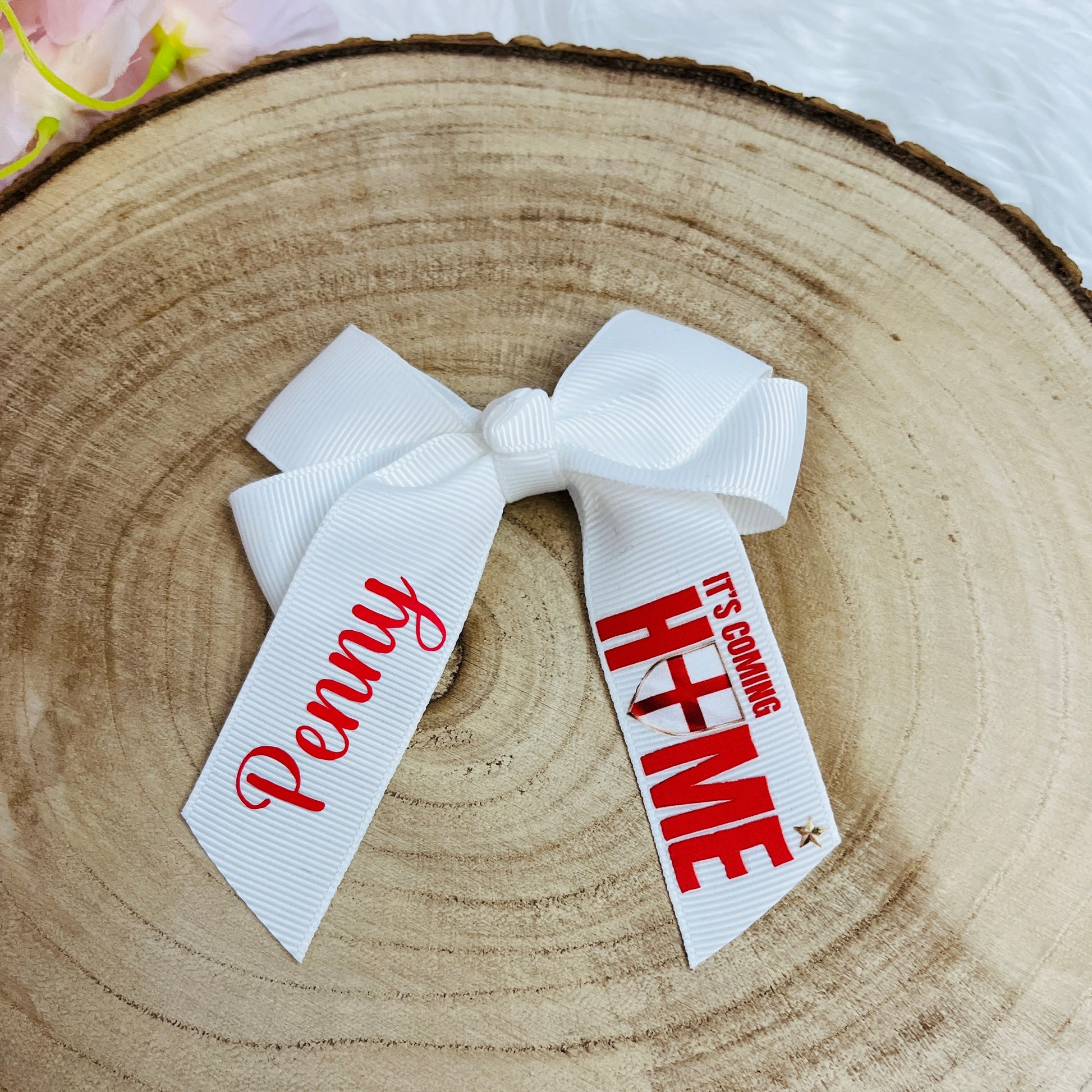White hair bow with personalised name and 'It's Coming Home' World Cup 26 decal on opposite tail against a wooden surface