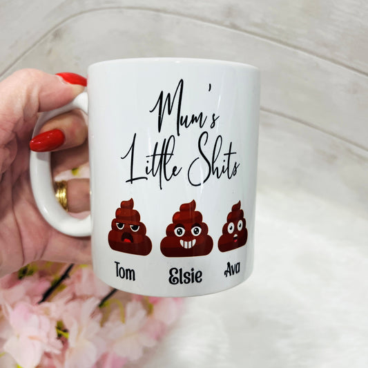 A novelty white mug with the text 'Mums little Shits' and three emojis with personalised names