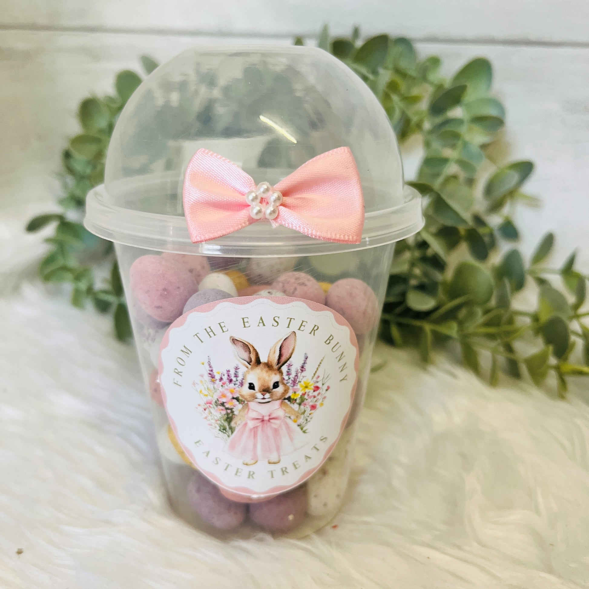 An Easter Dome Snack Pot featuring a plastic cup with a pink bunny wreath design and a pink bow on the lid, filled with various small snacks.