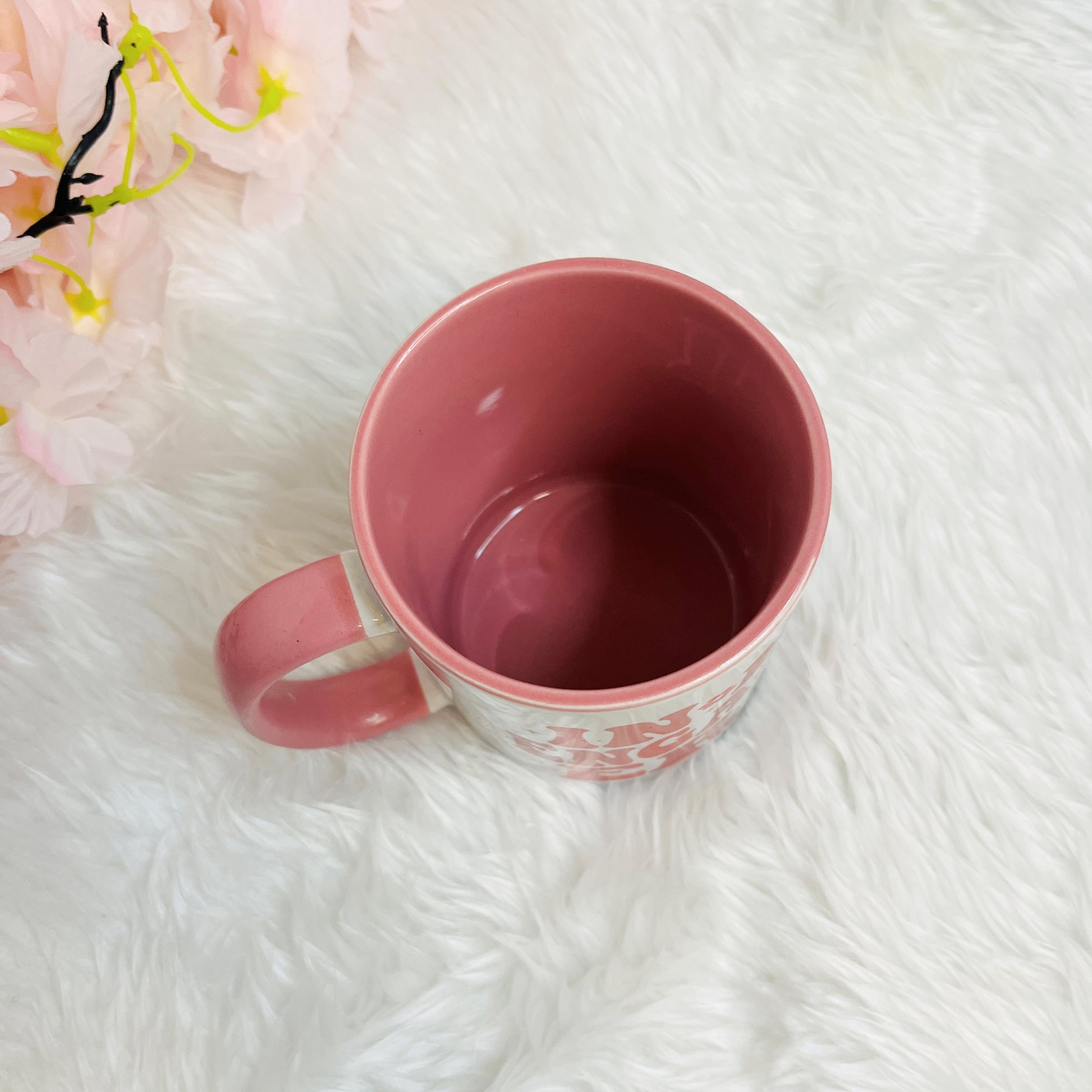 Inside of Pink mug on a white textured surface with pink flowers in the corner