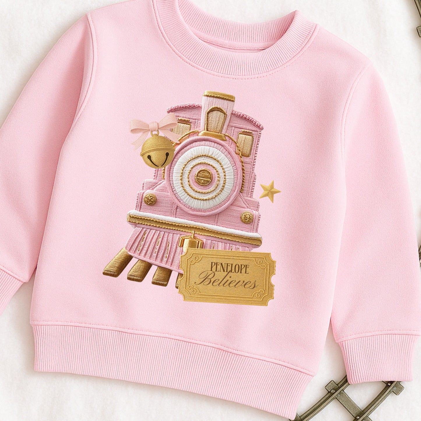 Pink Childs Jumper with an embroidered Train design and a golden ticket on a flat background