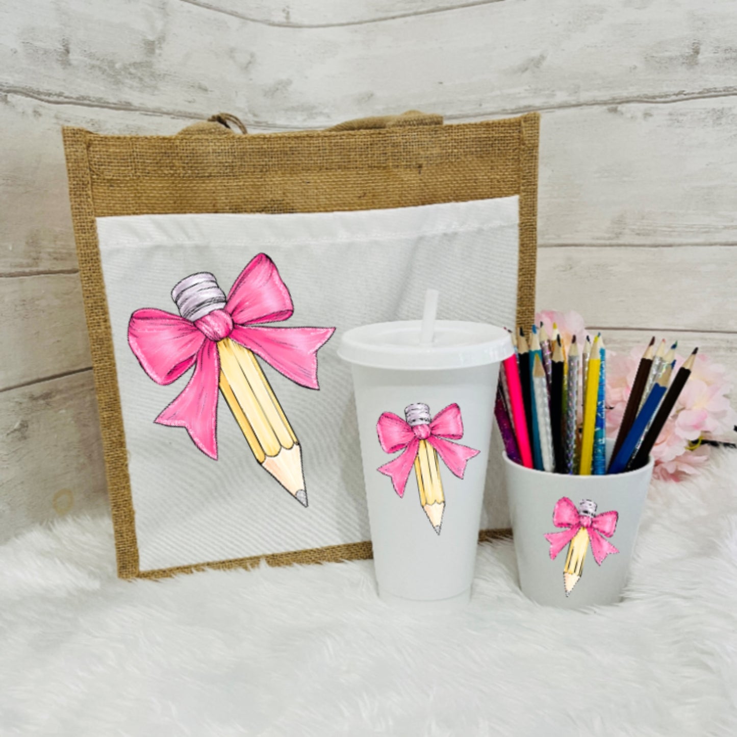 Set of stationery items including a bag, cups, and pencils with pink bow designs on a wooden surface.