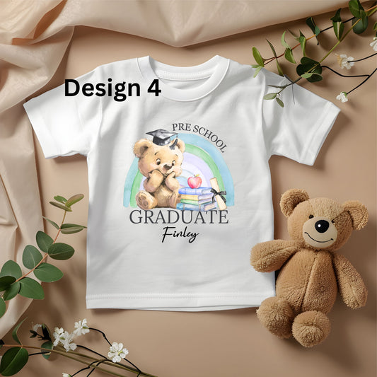 White t-shirt with teddy bear design and text, placed on a beige fabric background with a teddy bear and greenery.