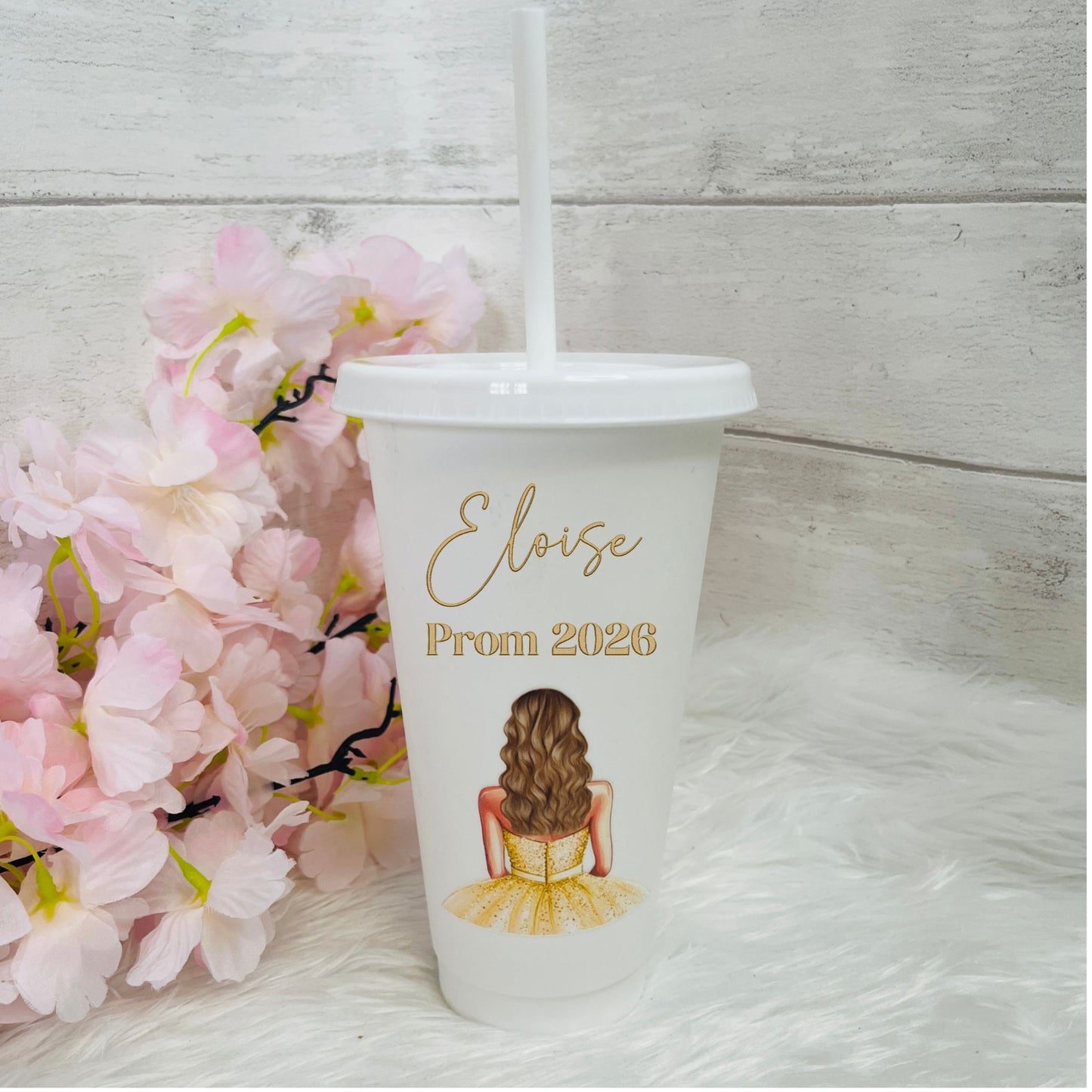 Prom-themed tumbler with a design of a girl in a yellow dress and 'Eloise Prom 2026' text, placed against a light wooden background with pink flowers.