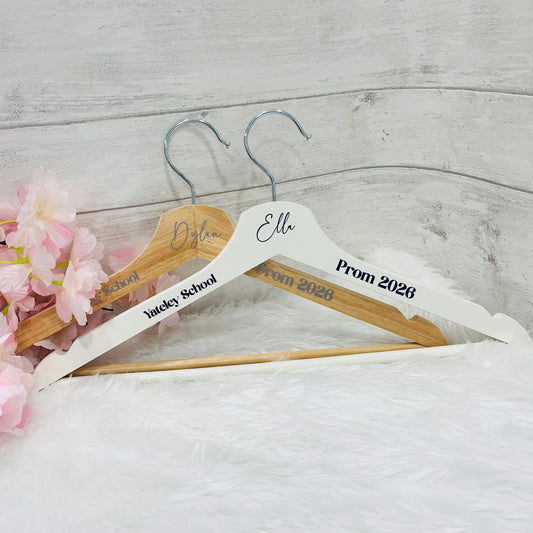 One white wooden hanger and one wooden hanger both with name, prom 2026 and school printed on them against a white background