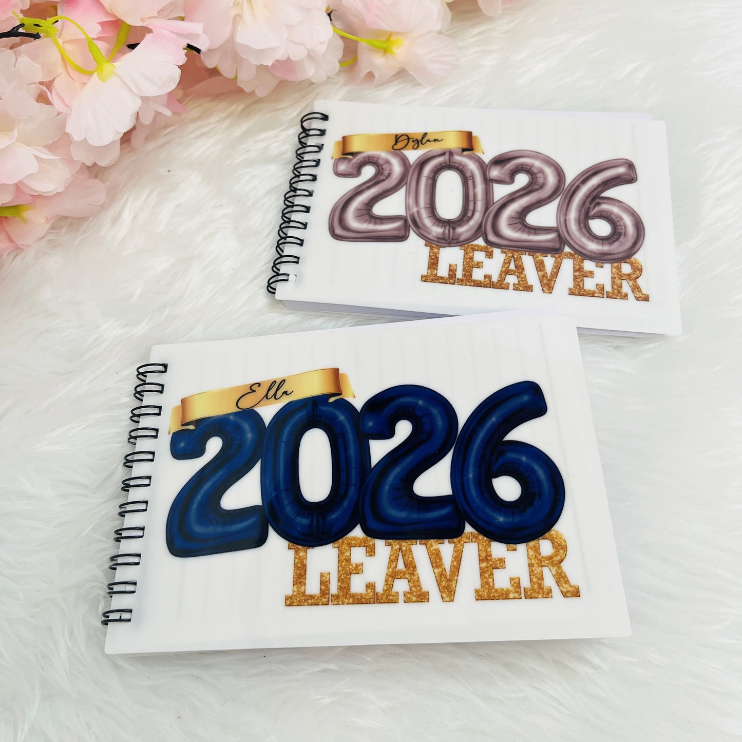 Two notebooks with '2026 Leaver' text on a white surface with pink flowers.
