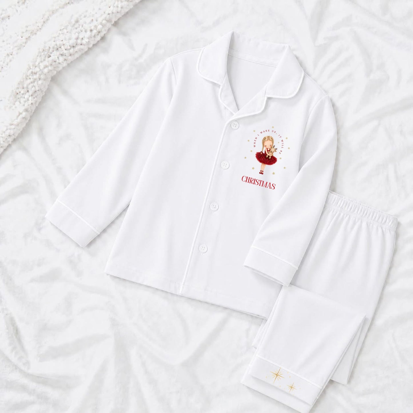 A white pajama set laid flat on a white textured background, featuring a long-sleeve button-front top with a ballerina dressed in a red tutu with long blonde plait and the text 'when i wake up it will be christmas'