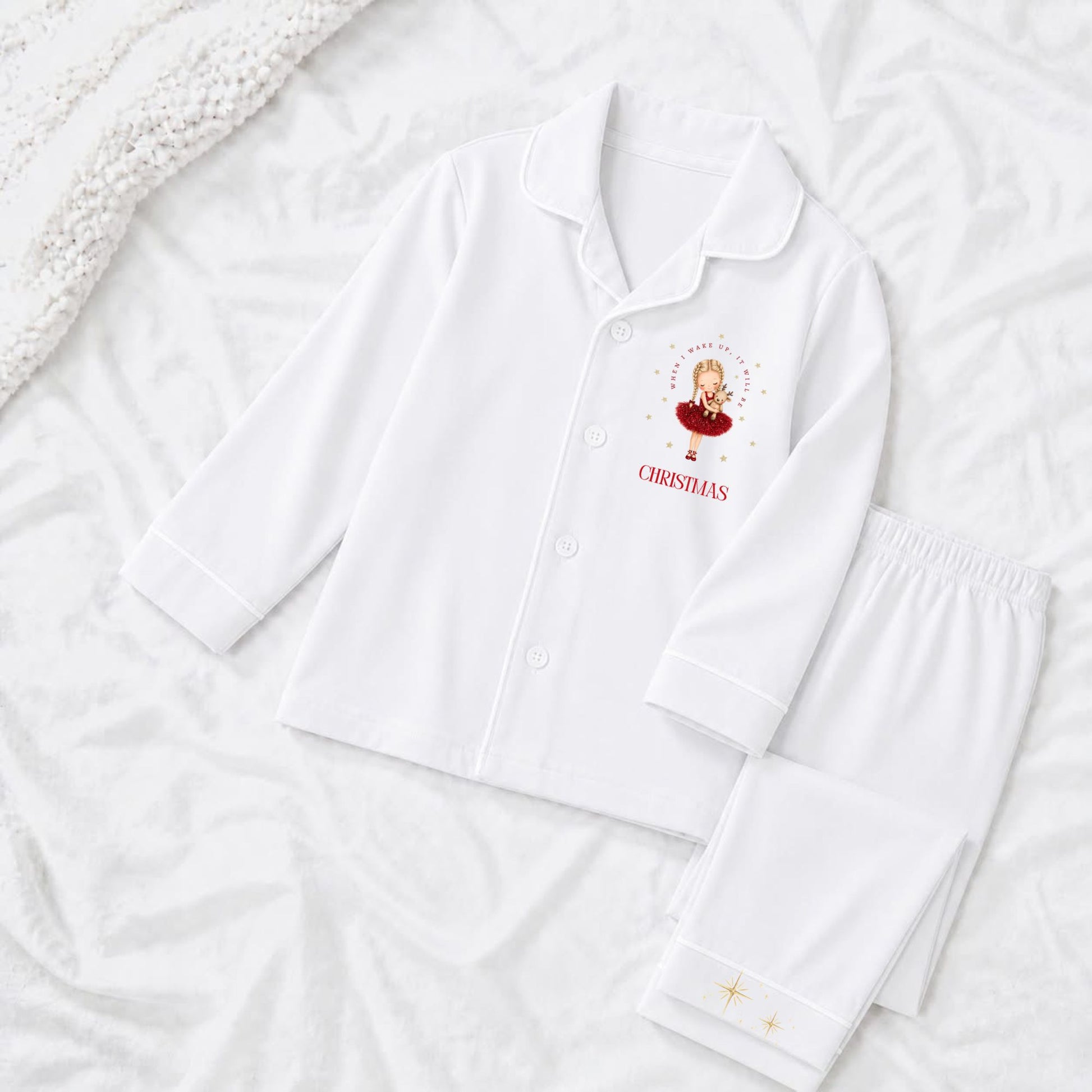 A white pajama set laid flat on a white textured background, featuring a long-sleeve button-front top with a ballerina dressed in a red tutu with long blonde plait and the text 'when i wake up it will be christmas'