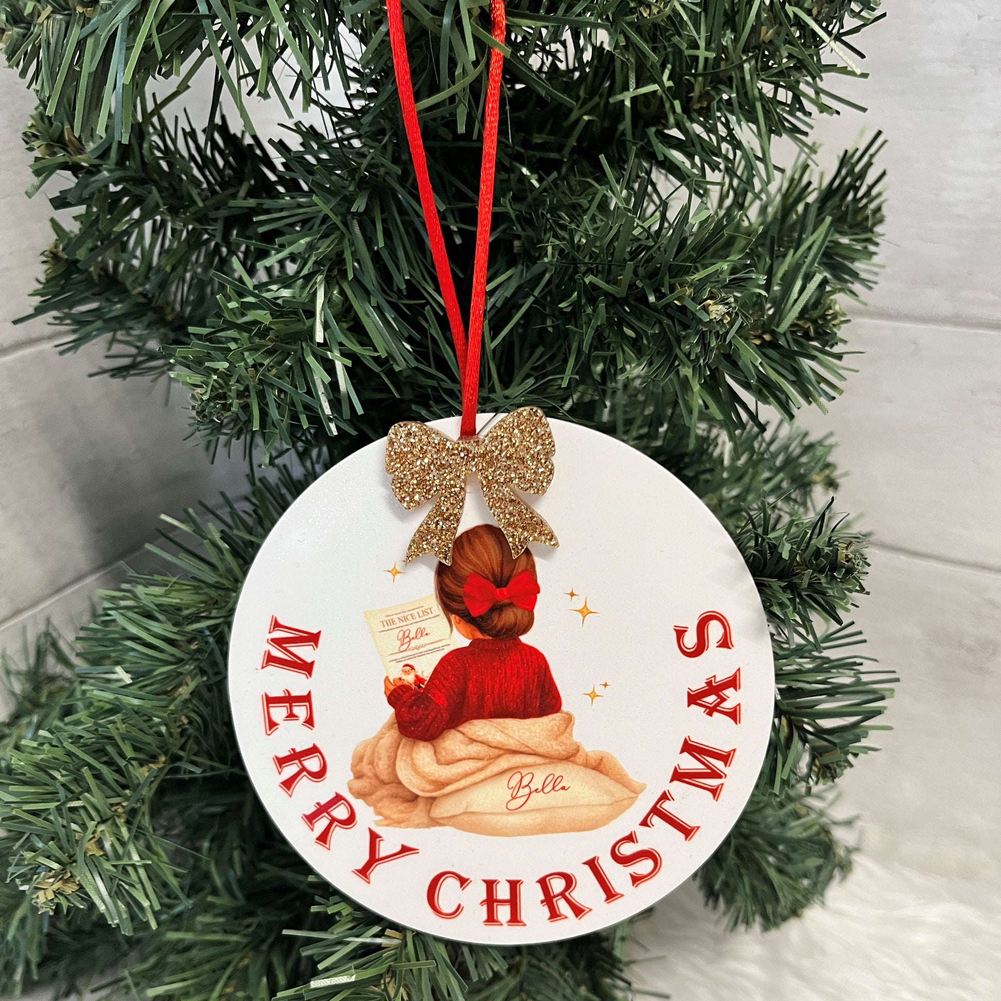 Christmas Acrylic ornament with a little girl design and the words 'Merry Christmas' round the bottom of the ornament with an acrylic glitter gold bow at the top and a red hanging ribbon 