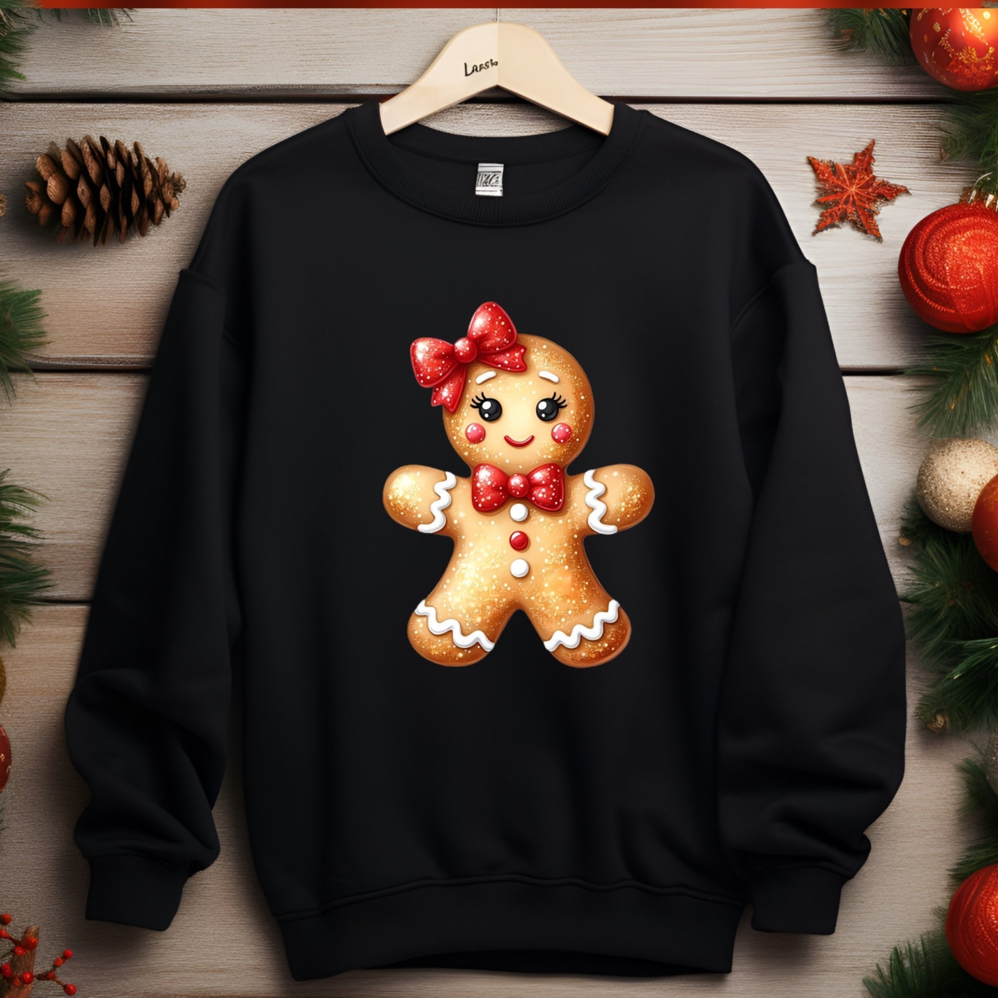 Black sweatshirt with a gingerbread girl design on a wooden surface with Christmas decorations.