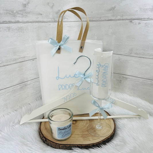 Gift set with frosted gift bag, wine glass, candle, and hanger on a wooden surface.