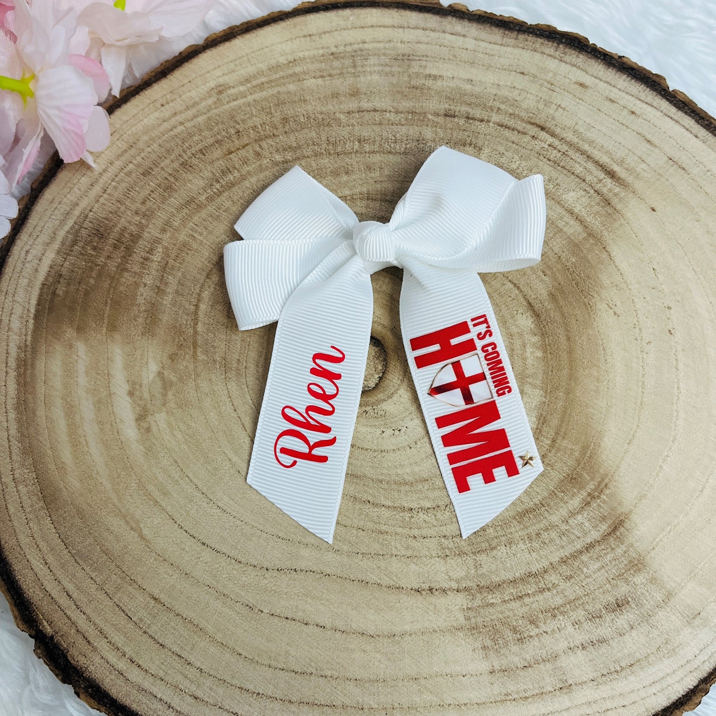 White hair bow with personalized ribbons on a wooden surface