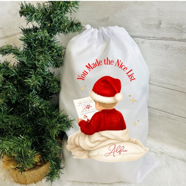 White drawstring bag with a printed design of a child in a Santa hat and jumper, next to a small Christmas tree.
