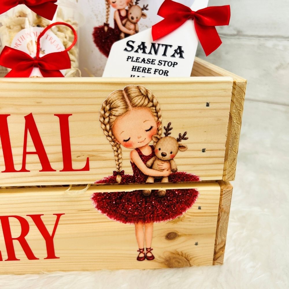 A wooden gift box with a Christmas illustration of a girl in a red tutu holding a reindeer, with red ribbon bows and a Santa-themed tag visible on top.