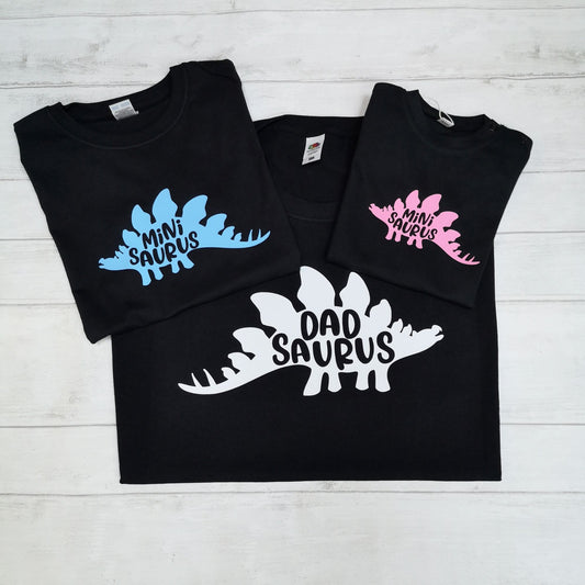 Black t-shirts with dinosaur-themed text on a light wooden surface