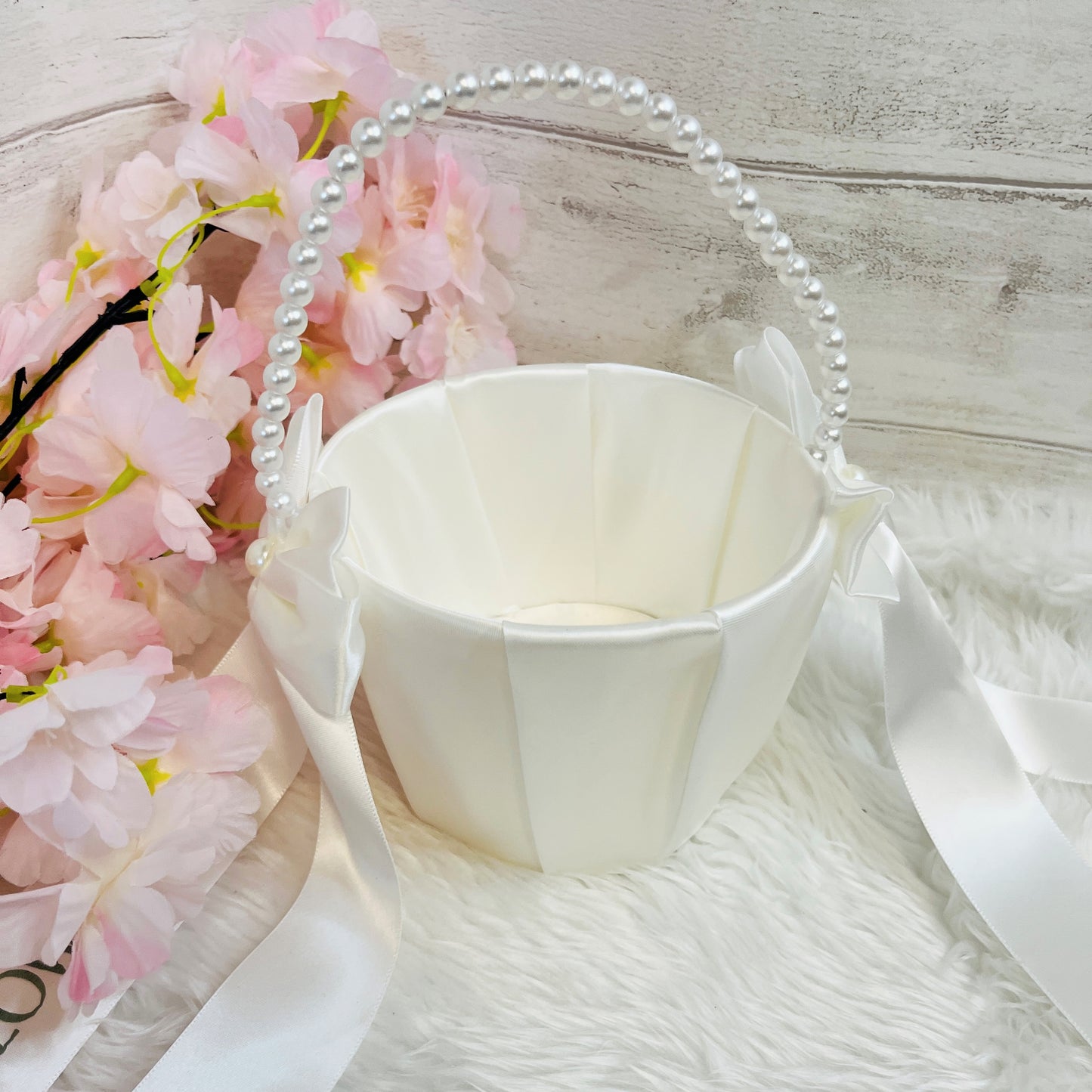 White flower girl basket with pink flowers and a pearl handle on a light wooden surface.