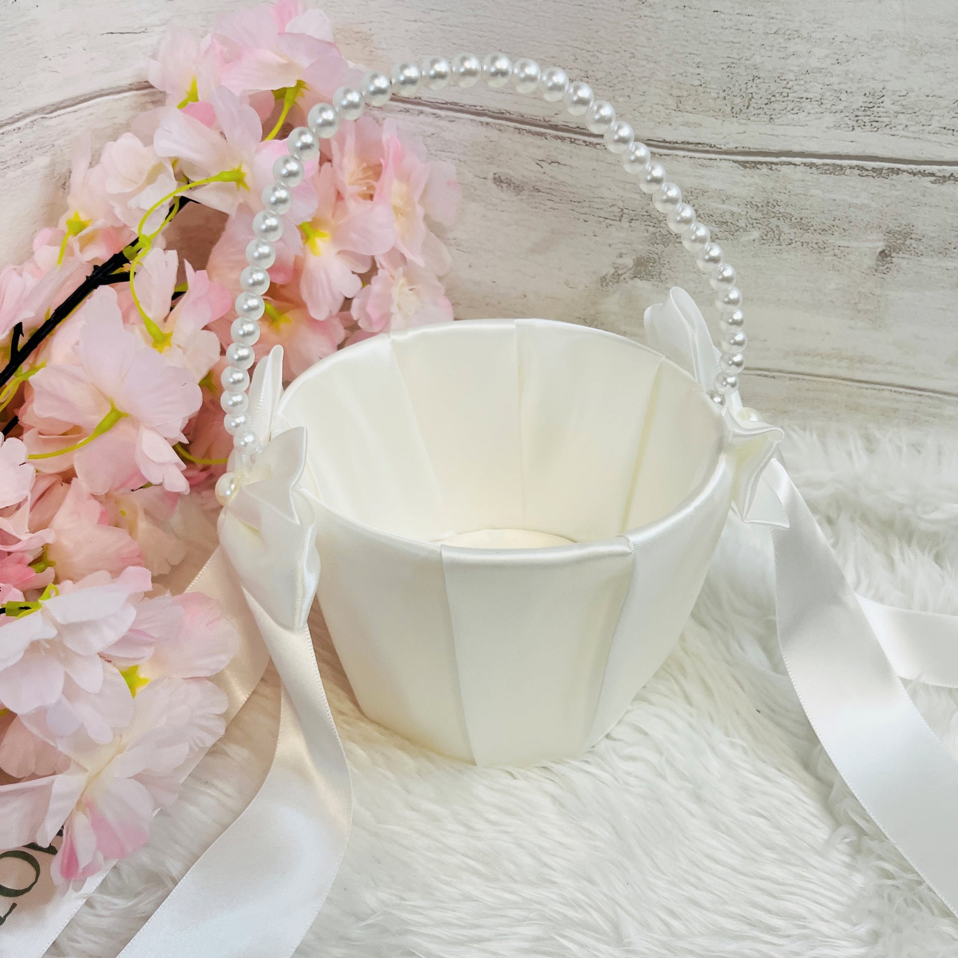White flower girl basket with pink flowers and a pearl handle on a light wooden surface.