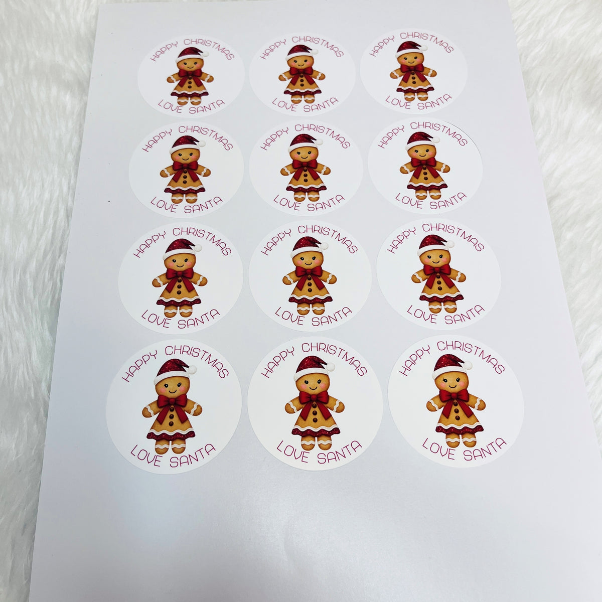 A sheet of round Christmas-themed stickers featuring gingerbread girls in red and brown outfits with 'HAPPY CHRISTMAS LOVE SANTA' text, arranged on a white background.