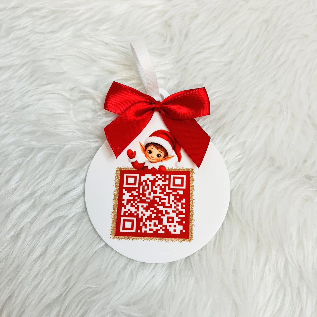 A white acrylic Christmas ornament with a red ribbon bow and a printed red-and-white QR code, placed on a white faux-fur surface.