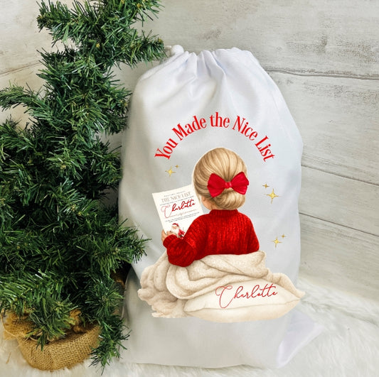 White drawstring bag with a Christmas-themed design of a child in a red sweater and bow, next to a small Christmas tree.