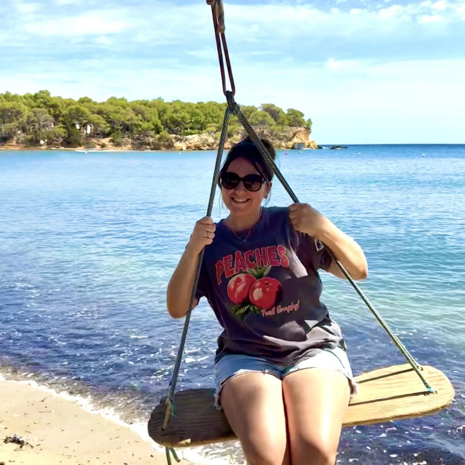 Person sitting on a swing by the beach with ocean and trees in the background