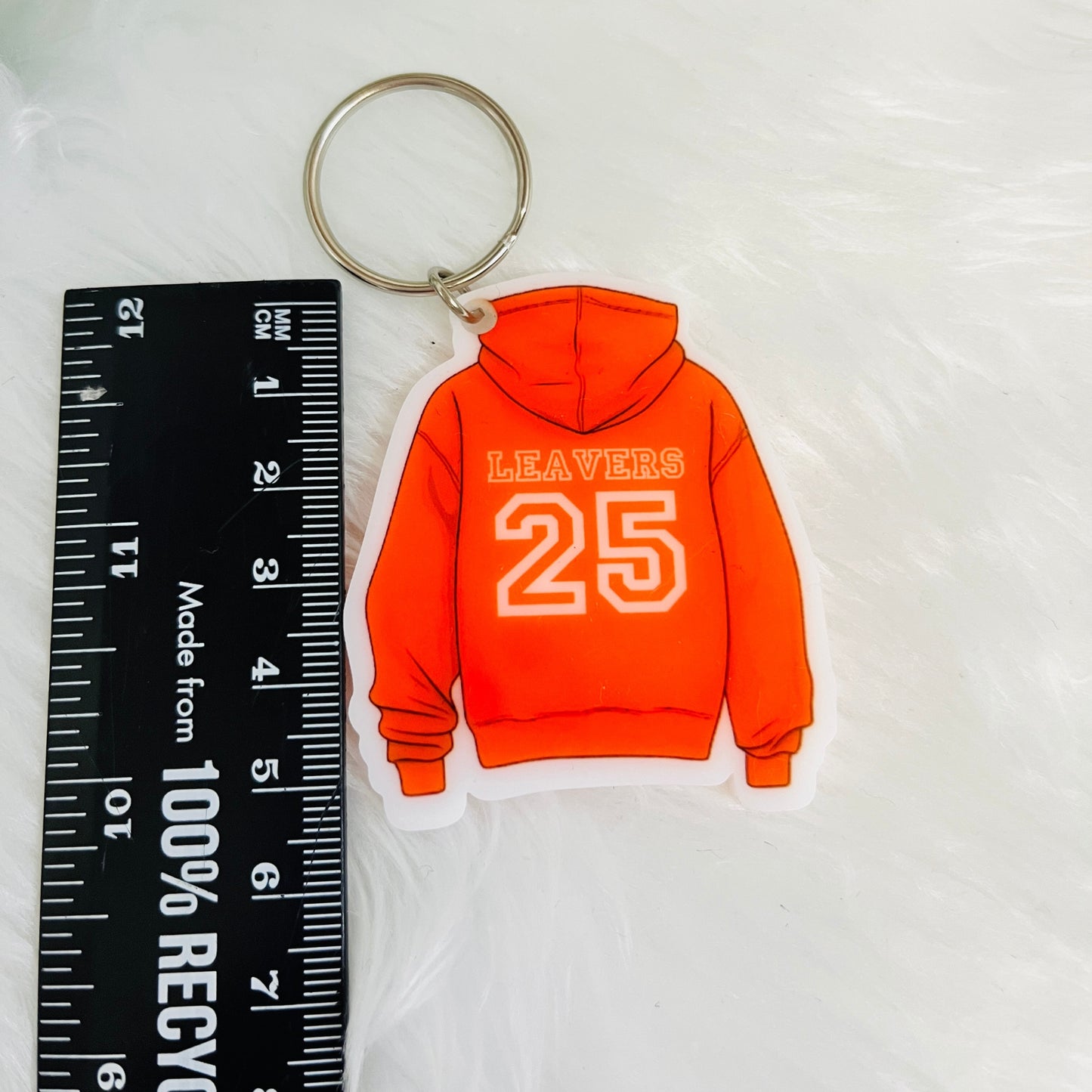 Orange hoodie keychain with 'LEAVERS 25' text next to a ruler on a white background
