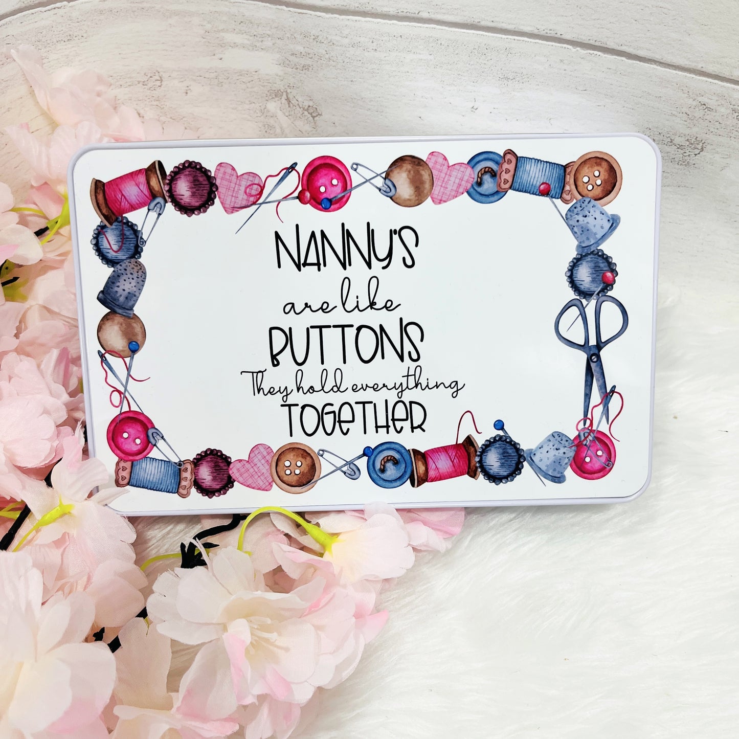 A white metal sweet tin with the text 'nannys are like buttons, they hold everything together' on the front with a sewing themed design around the edge