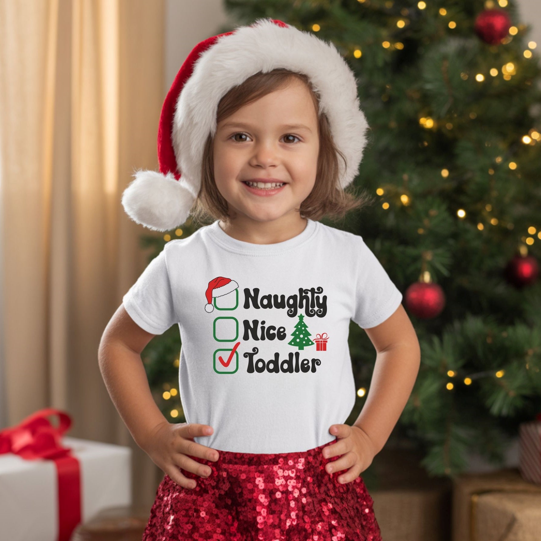 a small child wearing a santa hat and a white T-shirt with the texr ' naughty nice, toddler' on the front