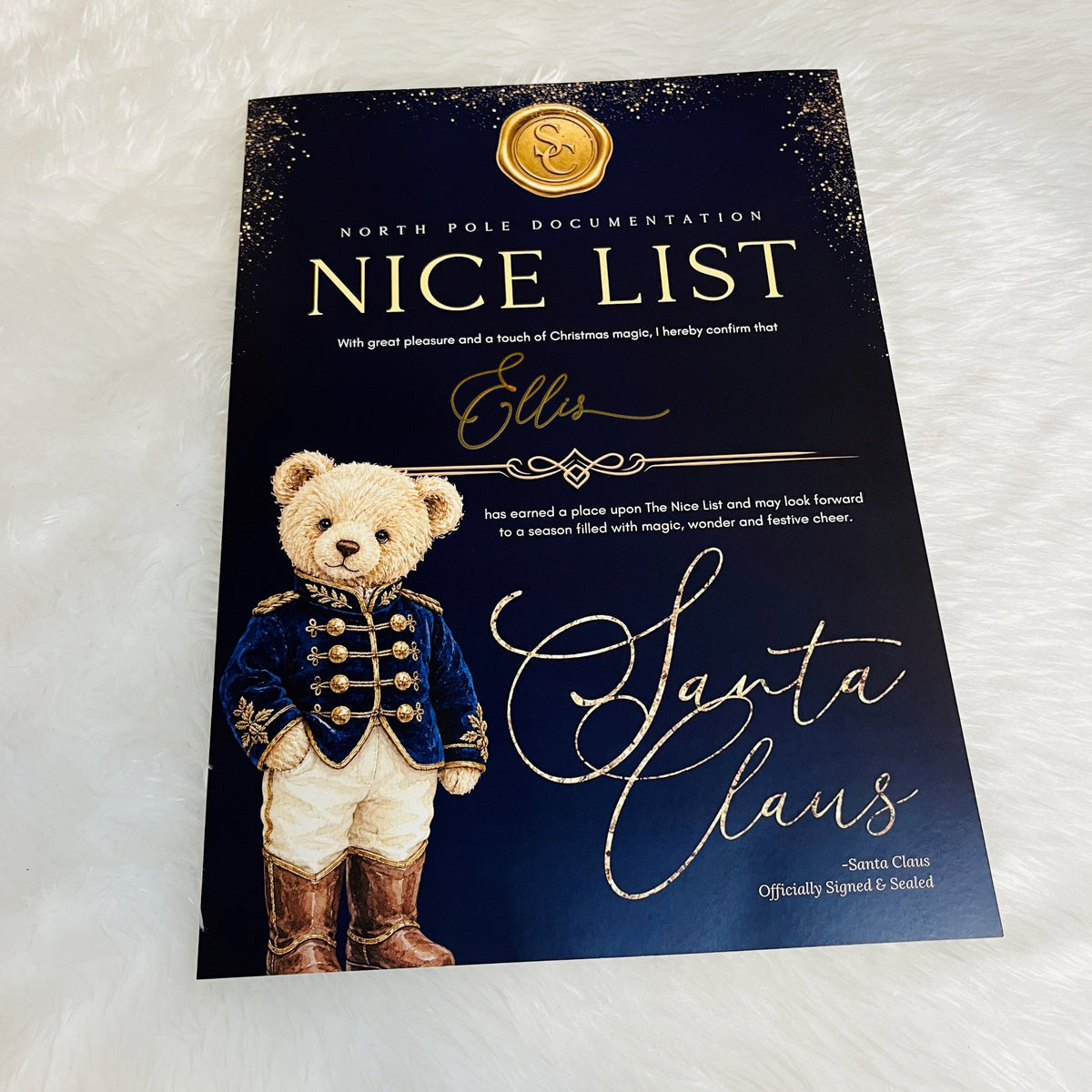 A printed card  titled 'Nice List' from North Pole Documentation, featuring a teddy bear dressed as Santa Claus on a dark navy background with gold glitter accents and gold script text.