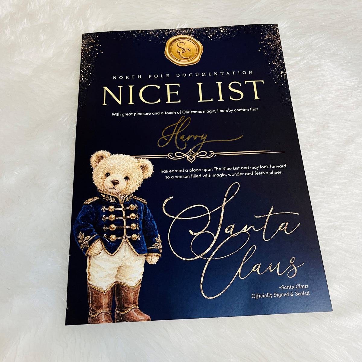A printed card titled "Nice List" from North Pole Documentation, featuring a teddy bear dressed as Santa Claus on a dark navy background with gold glitter and gold lettering. The card is photographed on a white faux-fur surface.