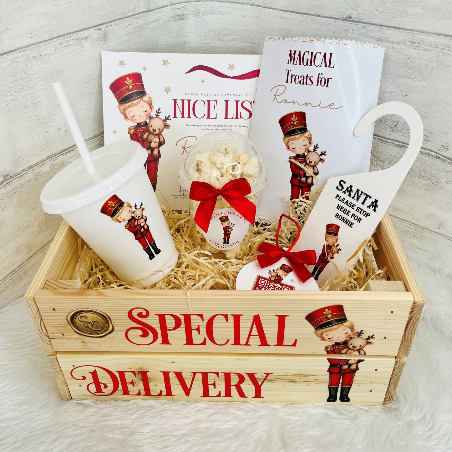 A Christmas-themed wooden crate  labeled 'SPECIAL DELIVERY.' The set includes a white cup with a straw, a small popcorn bowl tied with a red ribbon, printed cards, a Santa sign, and nutcracker illustrations.