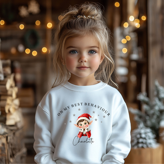 Child wearing a white sweatshirt with a Christmas-Elf-themed design in a festive setting.