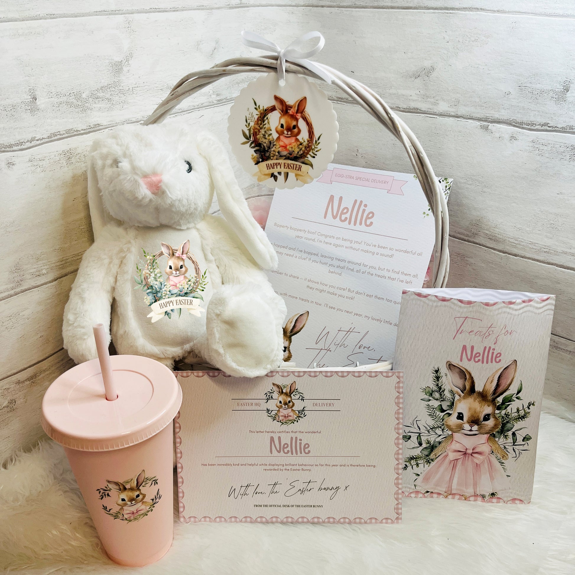 Pink Easter basket with plush bunny, tumbler, and cards on a white surface